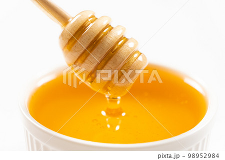 Liquid natural bee honey in a white ceramic bowl with a wooden spoon. 98952984