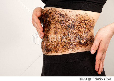 A woman applies a coffee scrub to the abdomen, anti-cellulite massage and peeling of the skin of the abdomen. 98953158