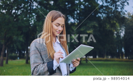 A young girl walks with a tablet in the park. 98954014
