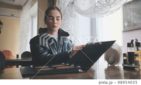 A young girl sits in a cafe and opens the menu. A young girl sits in a cafe and opens the menu. 98954035