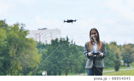 A cute girl controls a drone in the park. 98954045