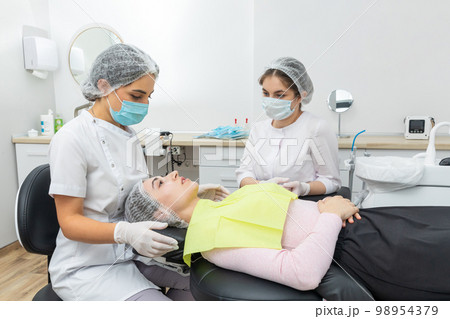 Dentist and assistant performing dental treatment inmodern dental clinic, patient laying in a chair Dentist and assistant performing dental treatment inmodern dental clinic, patient laying in a chair 98954379