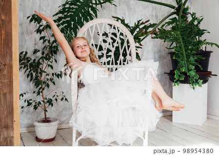 a girl in an elegant dress sits on a chair near green plants 98954380