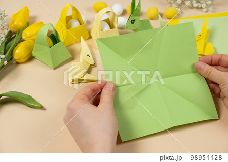Handicrafts from paper for Easter - origami, making figurines of Easter bunnies, hands close-up Handicrafts from paper for Easter - origami, making figurines of Easter bunnies, hands close-up 98954428
