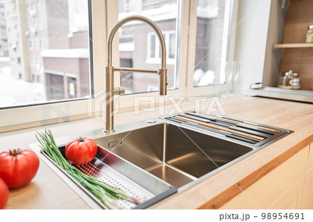 Stylish metallic crane at the kitchen. Sink faucet at the kitchen. Metal crane in close-up photo. Details of the interior of the kitchen in the house. 98954691