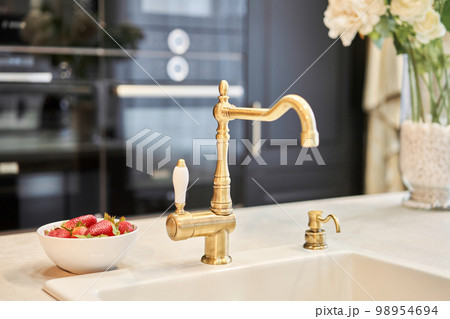 Stylish metallic crane at the kitchen. Sink faucet at the kitchen. Metal crane in close-up photo. Details of the interior of the kitchen in the house. Stylish metallic crane at the kitchen. Sink faucet at the kitchen. Metal crane in close-up photo. Details of the interior of the kitchen in the house. 98954694