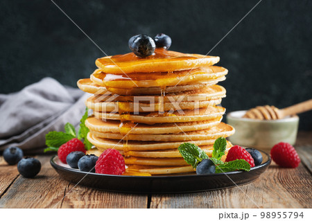 Delicious pancakes, with fresh blueberries, raspberry and maple syrup or honey on a dark background 98955794