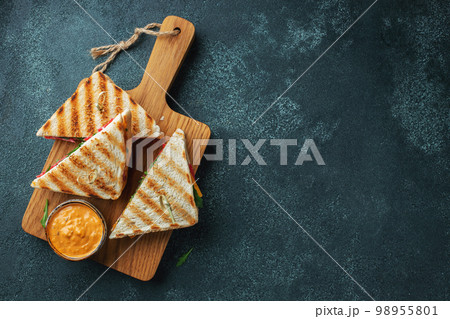 Four homemade sandwiches with sausage, cheese and arugula on a dark concrete background 98955801