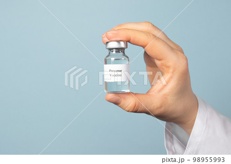 A doctor or laboratory technician keeps the Prevenar vaccine on a blue background. Vaccination against pneumocococy, prevention of pneumonia in infants 98955993