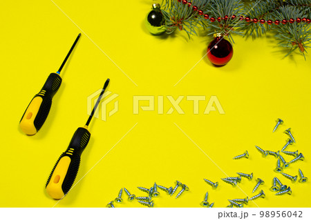 Screws and a screwdriver on a yellow background with a spruce branch. New year banner for hardware store and construction 98956042