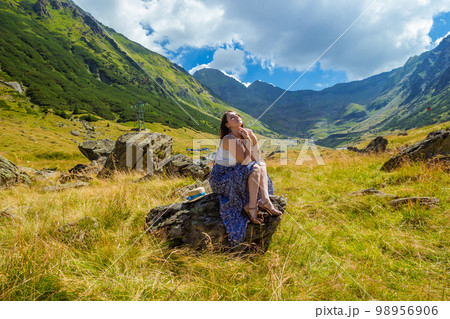 girl in long blue dress sits on a rock in the mountains 98956906