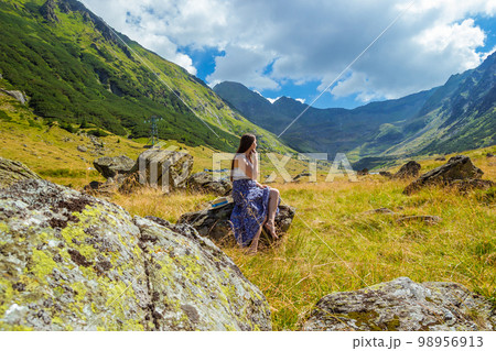 girl in long blue dress sits on a rock in the mountains girl in long blue dress sits on a rock in the mountains 98956913