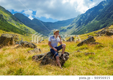 man in straw hat sits on a rock against the background of high mountains man in straw hat sits on a rock against the background of high mountains 98956915