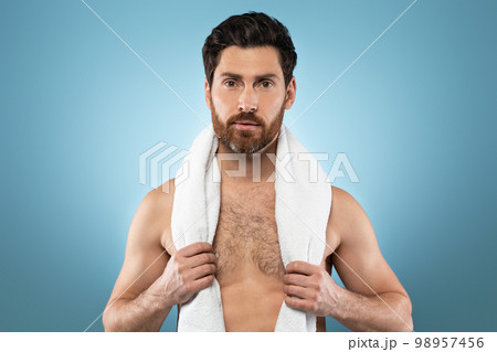 Portrait of handsome bearded man holding towel on shoulders, posing on blue background, studio shot Portrait of handsome bearded man holding towel on shoulders, posing on blue background, studio shot 98957456