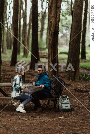 Glad young european man and lady tourists in jackets with backpack resting in forest, enjoy cold season outdoors Glad young european man and lady tourists in jackets with backpack resting in forest, enjoy cold season outdoors 98957480