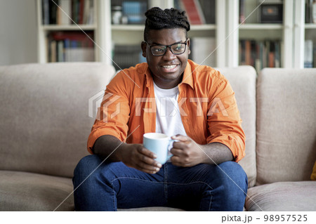 Relaxed african american chubby guy drinking tea at home 98957525