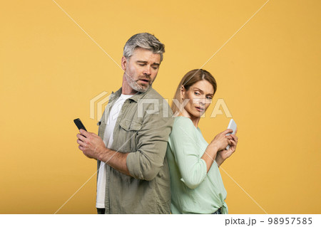Privacy concept. Middle aged caucasian man trying to look at his wife's smartphone, woman hiding screen of her gadget 98957585
