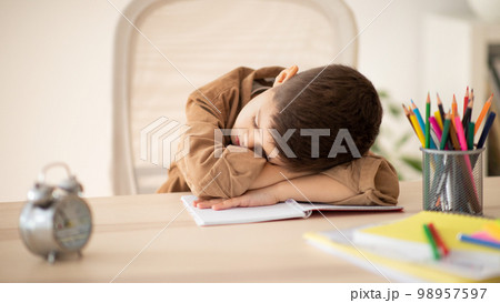 Bored unhappy tired caucasian little child sleeping at table, suffering from homework in room 98957597