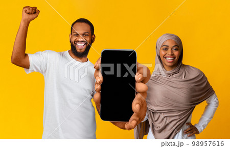 Overjoyed black muslim couple showing big blank smartphone with empty screen 98957616