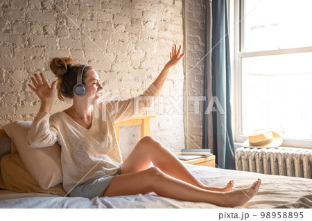 Young handsome woman listening to music with headphones in modern bedroom with brick wall 98958895