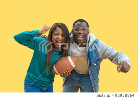 Excited ethnic diversity couple enjoying american football together isolated on yellow background  98958964