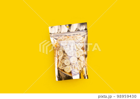 Banana slice chips in package bag on yellow background. 98959430