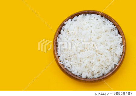Wooden bowl of rice on yellow background. Wooden bowl of rice on yellow background. 98959487