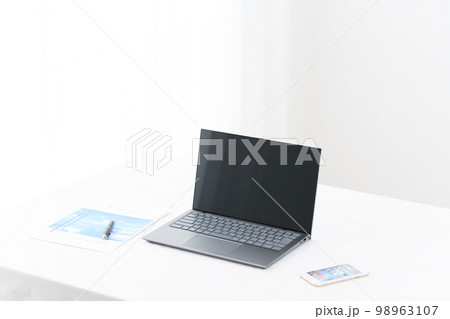白いテーブルんの上にあるノートパソコンとスマホと資料 98963107