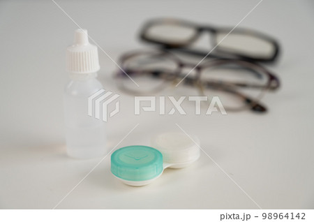 Two pairs of glasses lenses and contact drops in the eyes on a white table.  98964142