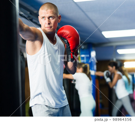 Male sportsman practicing boxing punches with punching bag Male sportsman practicing boxing punches with punching bag 98964356