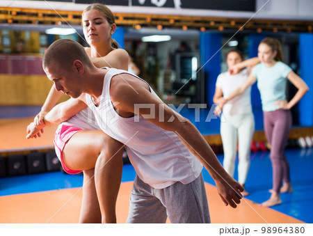 Girl performing elbow and knee strikes with arm hold to male sparring partner in gym 98964380