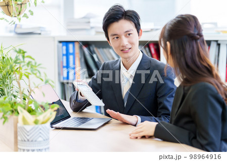 電卓を使って打ち合わせをする人々 98964916