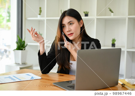 Attractive Asian businesswoman on the phone with her client while working in the office. 98967446
