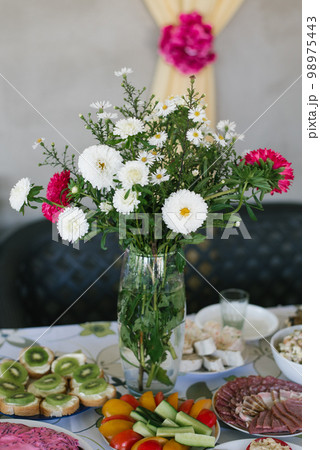 A bouquet of homemade asters in a glass vase in the decor of a country banquet 98975443