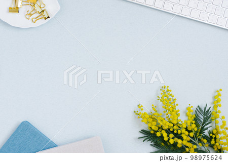 On a blue flat lay background with a yellow mimosa flower, keyboard notepad and stationery clips, a female floral desktop. The concept of a stylish spring morning. top view and copy space On a blue flat lay background with a yellow mimosa flower, keyboard notepad and stationery clips, a female floral desktop. The concept of a stylish spring morning. top view and copy space 98975624