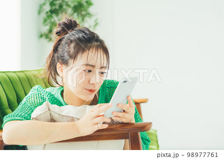 ソファに寝転がってスマホを見る女性 98977761