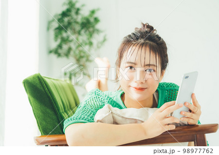 ソファに寝転がってスマホを見る女性 98977762
