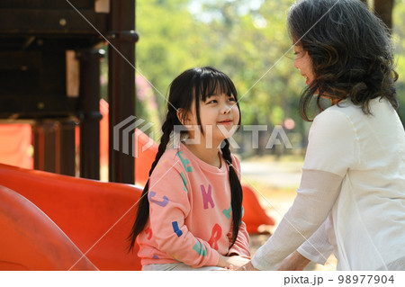 Happy child girl on slide, having fun on outdoor playground with grandma. Childhood and equipment of entertainment park Happy child girl on slide, having fun on outdoor playground with grandma. Childhood and equipment of entertainment park 98977904