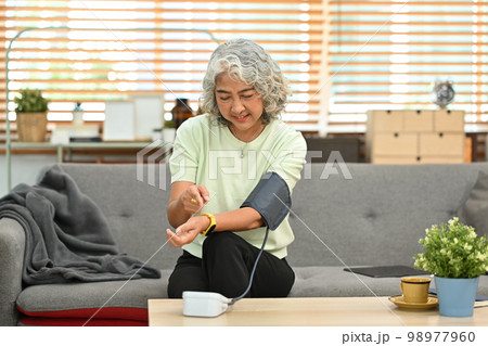 Senior woman checking blood pressure, sitting at a couch and using digital tonometer. Health and Medical concept 98977960