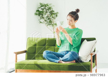 ソファに座ってスマホを見る女性 98977963