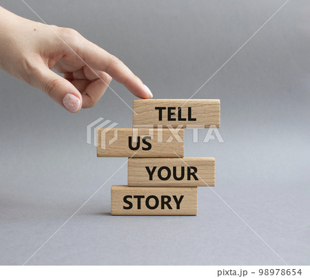 Tell us your story symbol. Concept words Tell us your story on wooden blocks. Beautiful grey background. Businessman hand. Business and Tell us your story concept. Copy space. 98978654