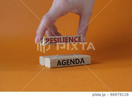 Resilience agenda symbol. Wooden blocks with words Resilience agenda. Businessman hand. Beautiful orange background. Business and Resilience agenda concept. Copy space. Resilience agenda symbol. Wooden blocks with words Resilience agenda. Businessman hand. Beautiful orange background. Business and Resilience agenda concept. Copy space. 98979116