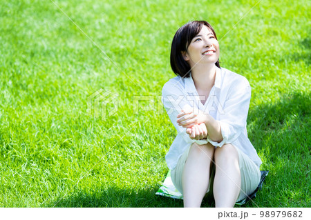 新緑の芝生で寛ぐ若い女性 98979682