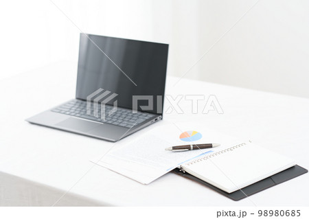 白いテーブルの上にノートパソコンとシステム手帳とペン（ペンピント）と資料のあるシーン 98980685