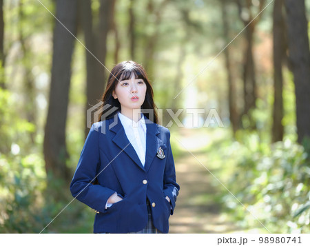 木漏れ日が降り注ぐ道で遠くを見ている女子高校生 98980741
