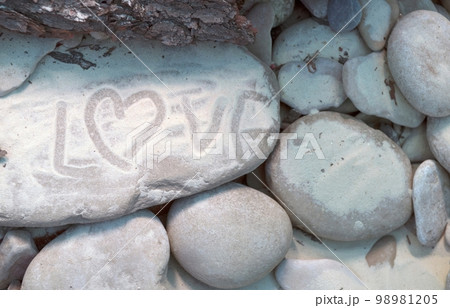 The word is love. Small stones and white sand. On the left side of the photo in the sand, the word love and a heart is displayed with a finger. 98981205