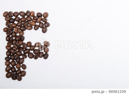 F is a capital letter of the English alphabet made up of natural roasted coffee beans that lie on a white background. Plenty of space to put text or pictures, top view and studio photography. 98981209