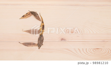 Three. The number three is composed of small autumn leaves on a light wooden textured table surface. View from above. 98981210