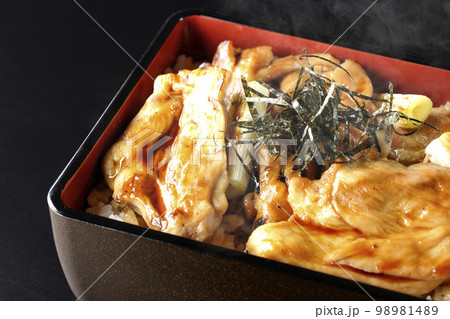 タレがたっぷりかかった熱々の炭火焼き鳥重を黒背景で撮影 98981489