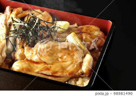 タレがたっぷりかかった熱々の炭火焼き鳥重を黒背景で撮影 98981490